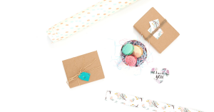 A wrapped gift, wrapping paper and sweets against a white background.